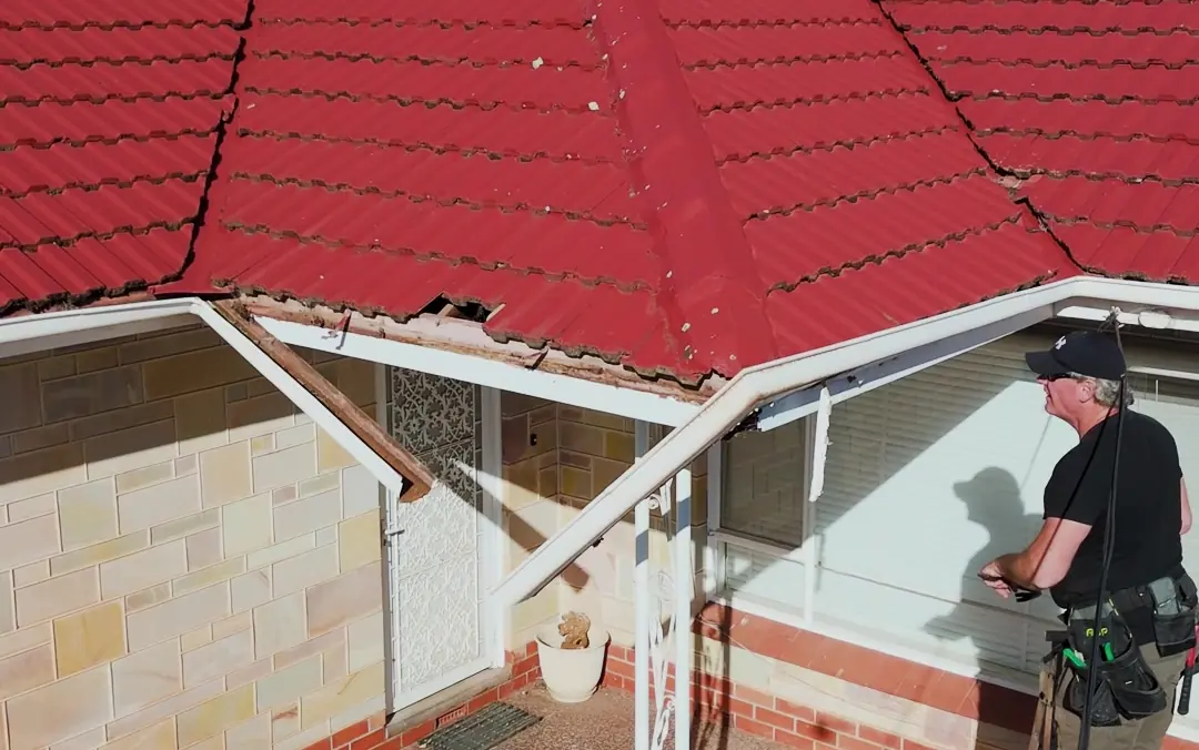 A red-tiled home with a broken eave corner, mid-repair