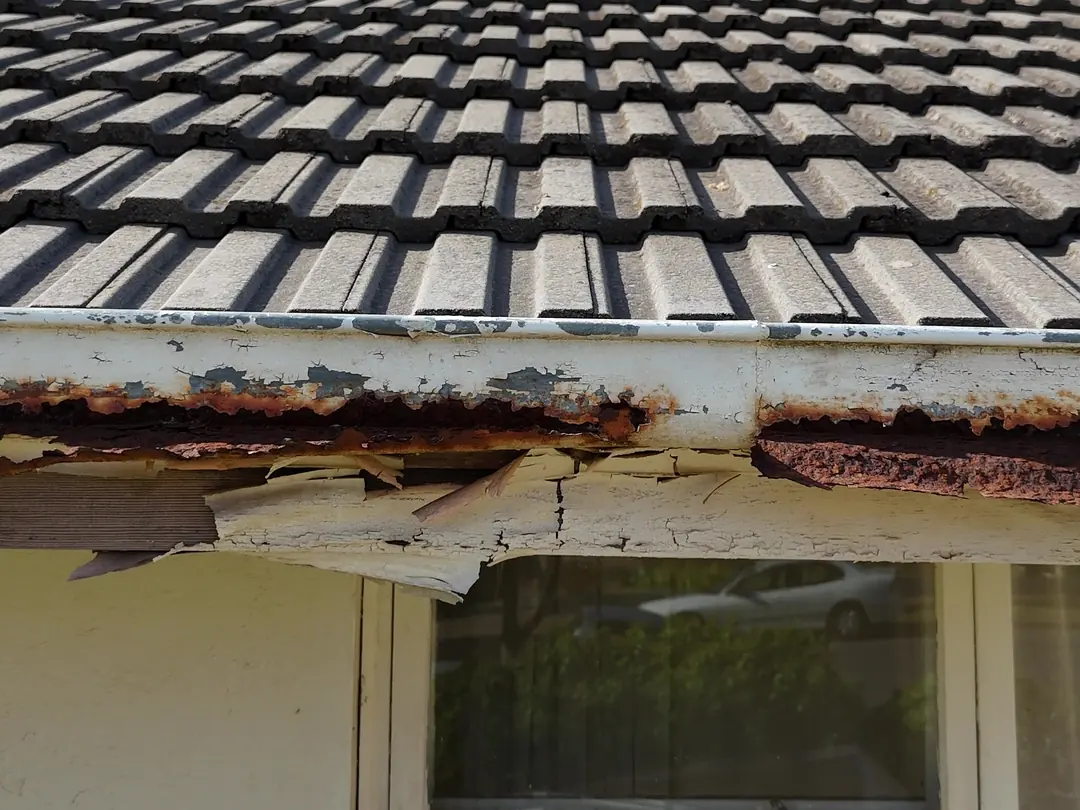 Before: rusted gutter and flaking fascia under old concrete tiles