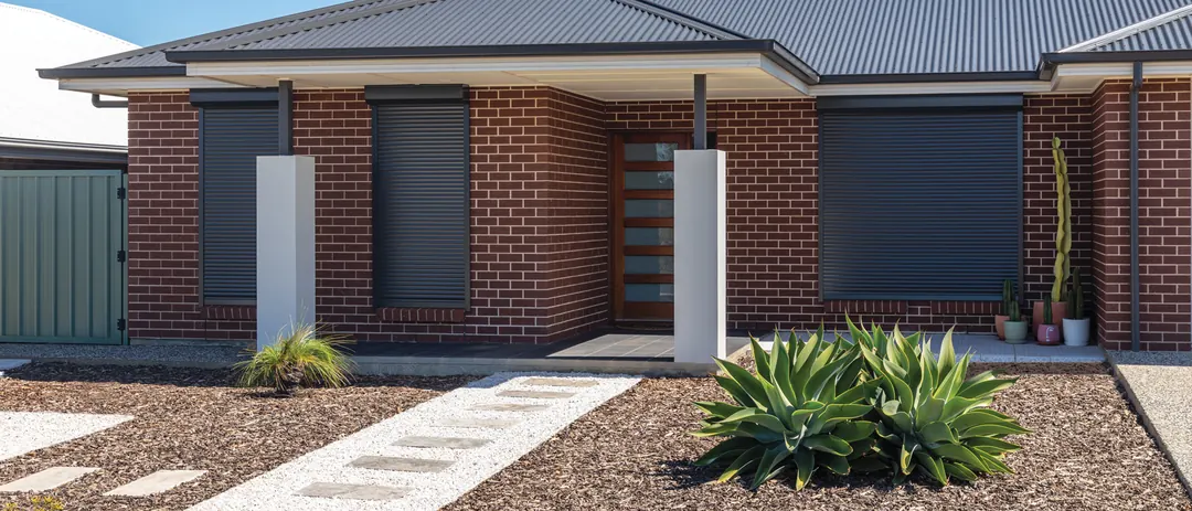 Charcoal roller shutters on the front windows of a brick home (supplier photo)
