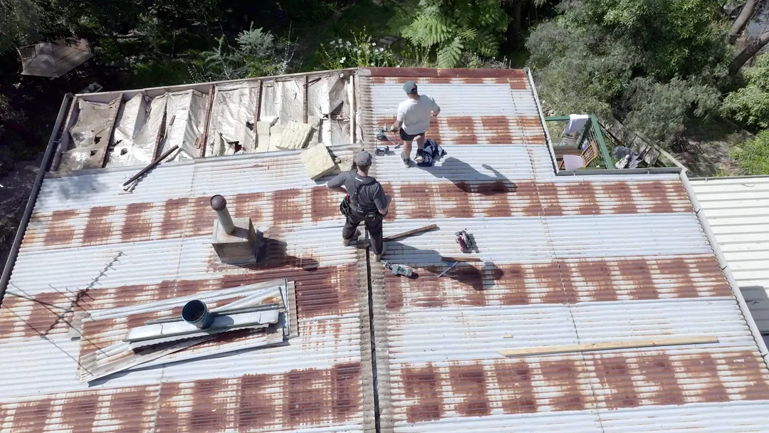 Two of the crew stripping a rusted corrugated iron roof back to the battens