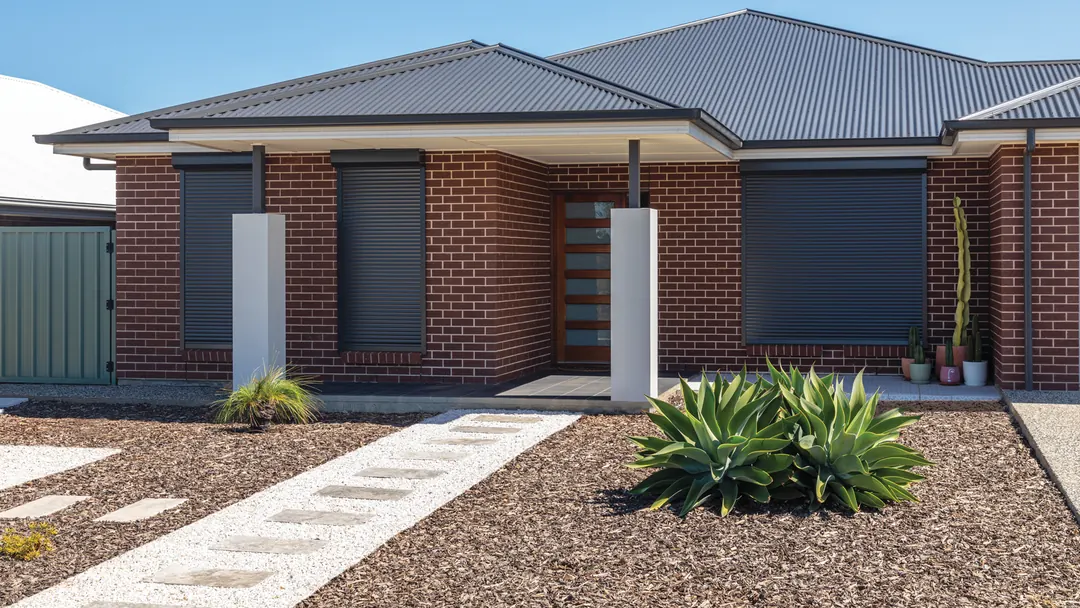 Charcoal roller shutters on the front windows of a brick home (supplier photo)